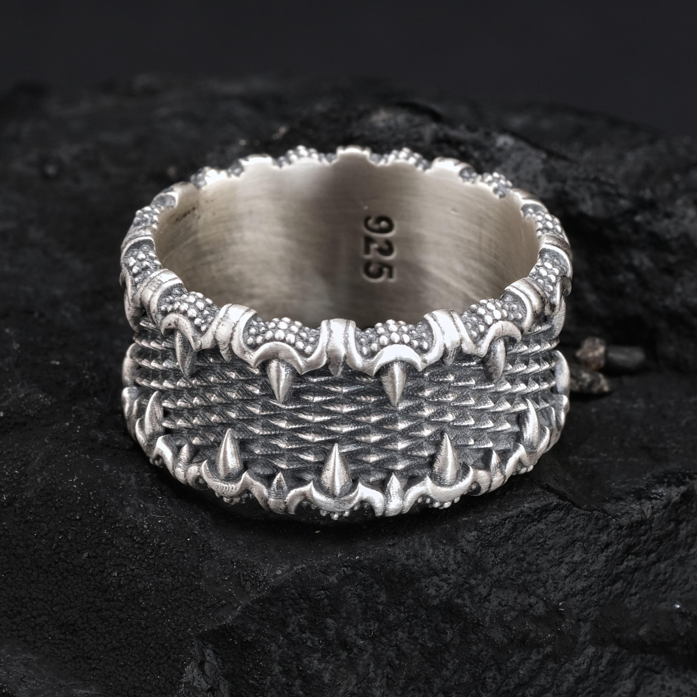 A silver ring with a textured, intricate design sits on a dark surface.
