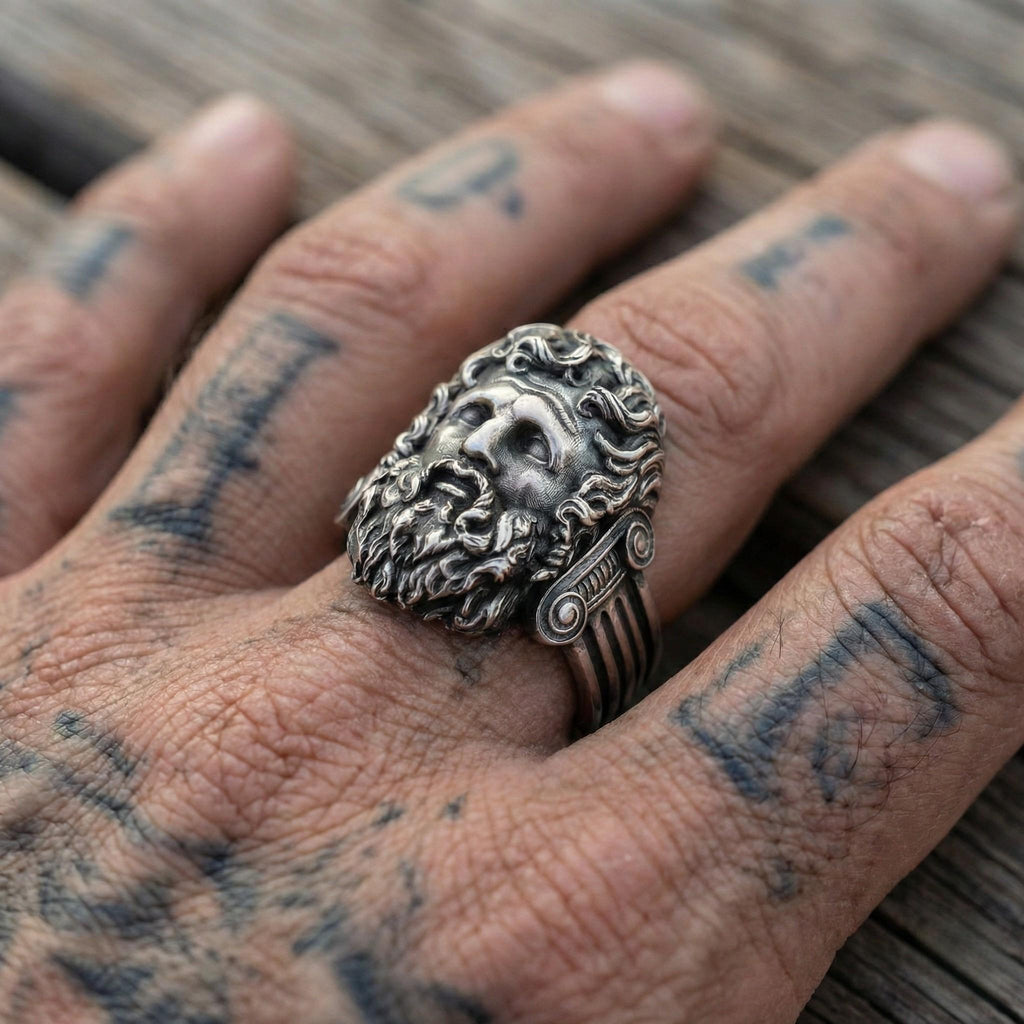 A close-up image of a person's hand wearing a large, ornate ring with a detailed, sculpted face design.