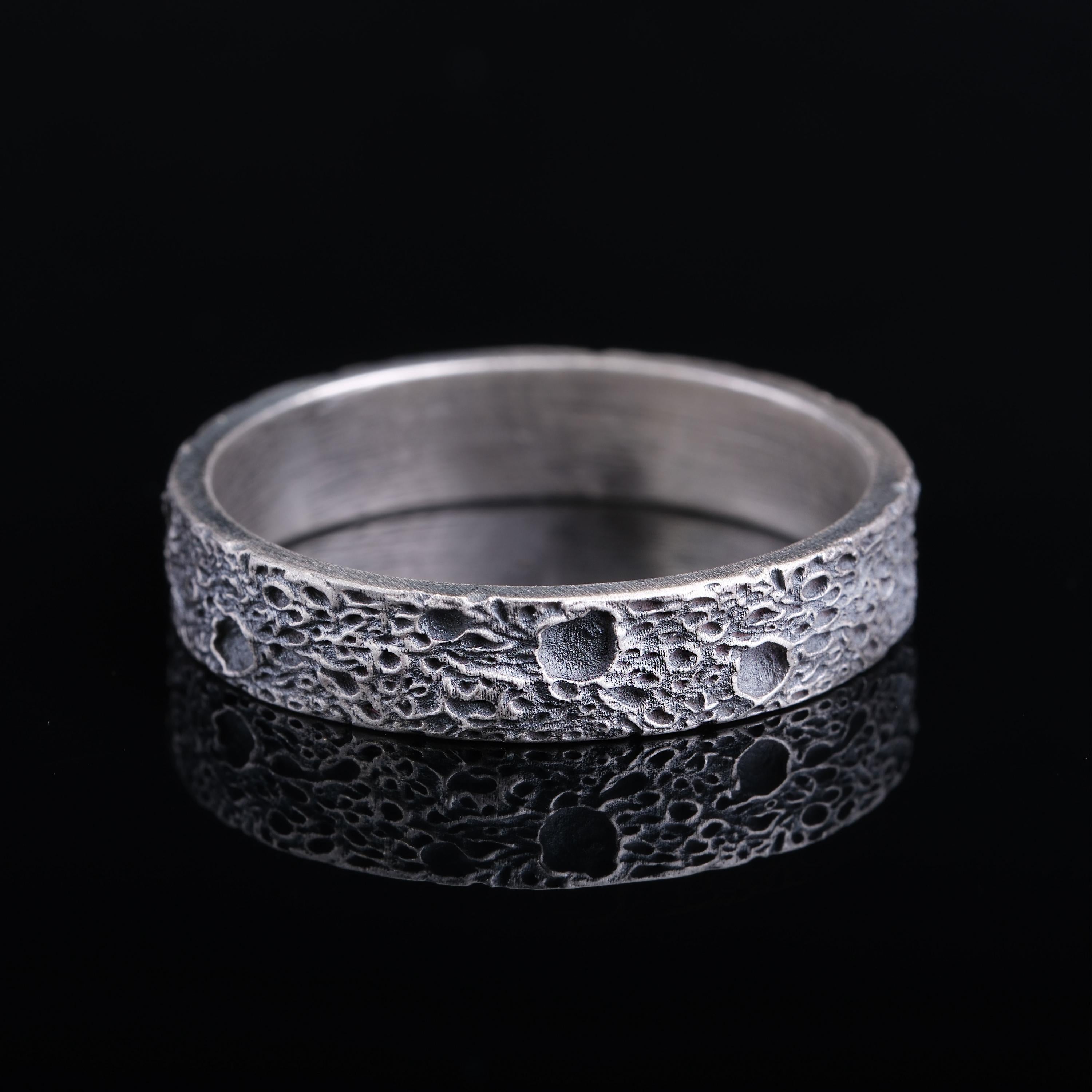 A silver ring with a textured surface, resembling the surface of the moon, is shown against a black background.
