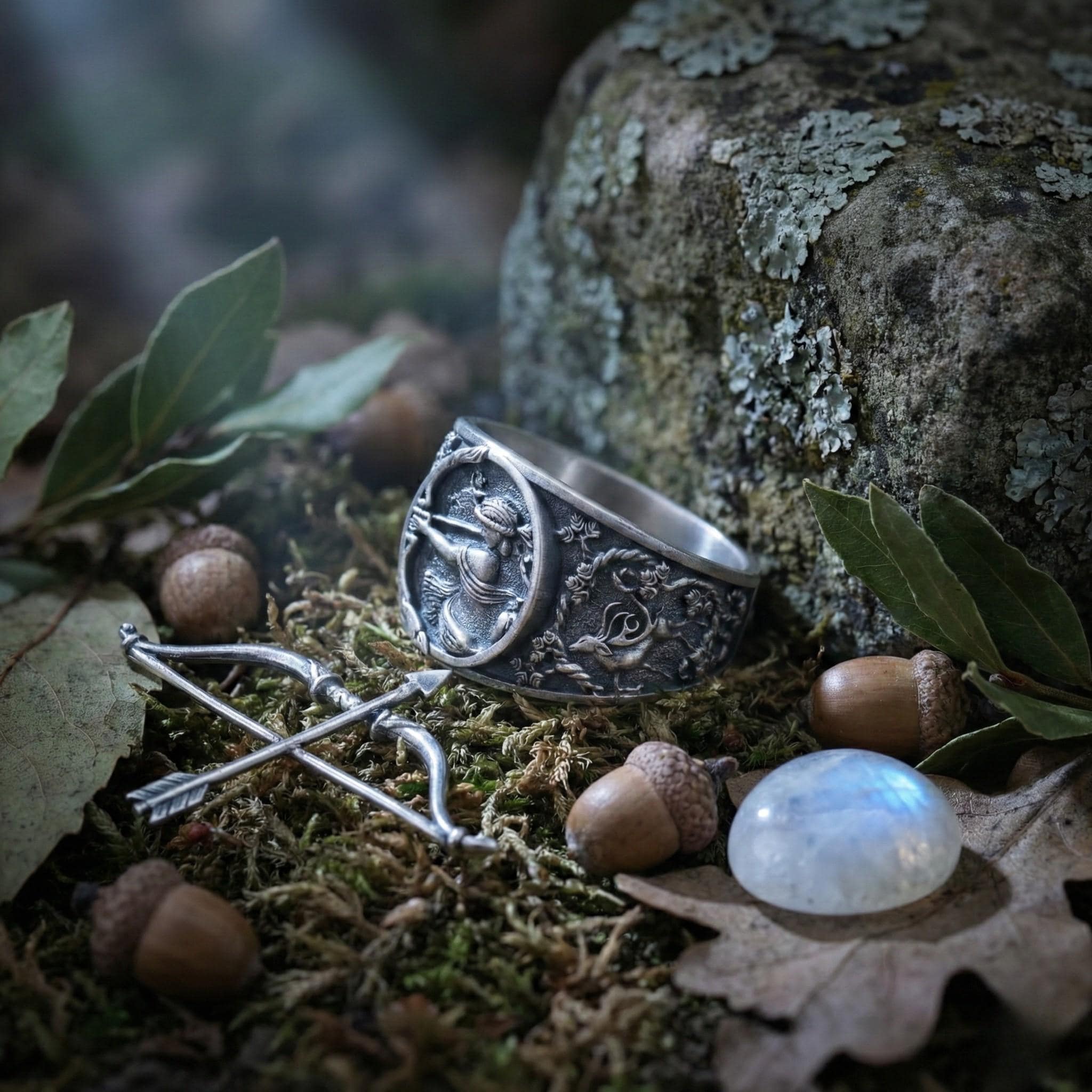a ring with a carved design, surrounded by various natural elements such as acorns, leaves, and moss.