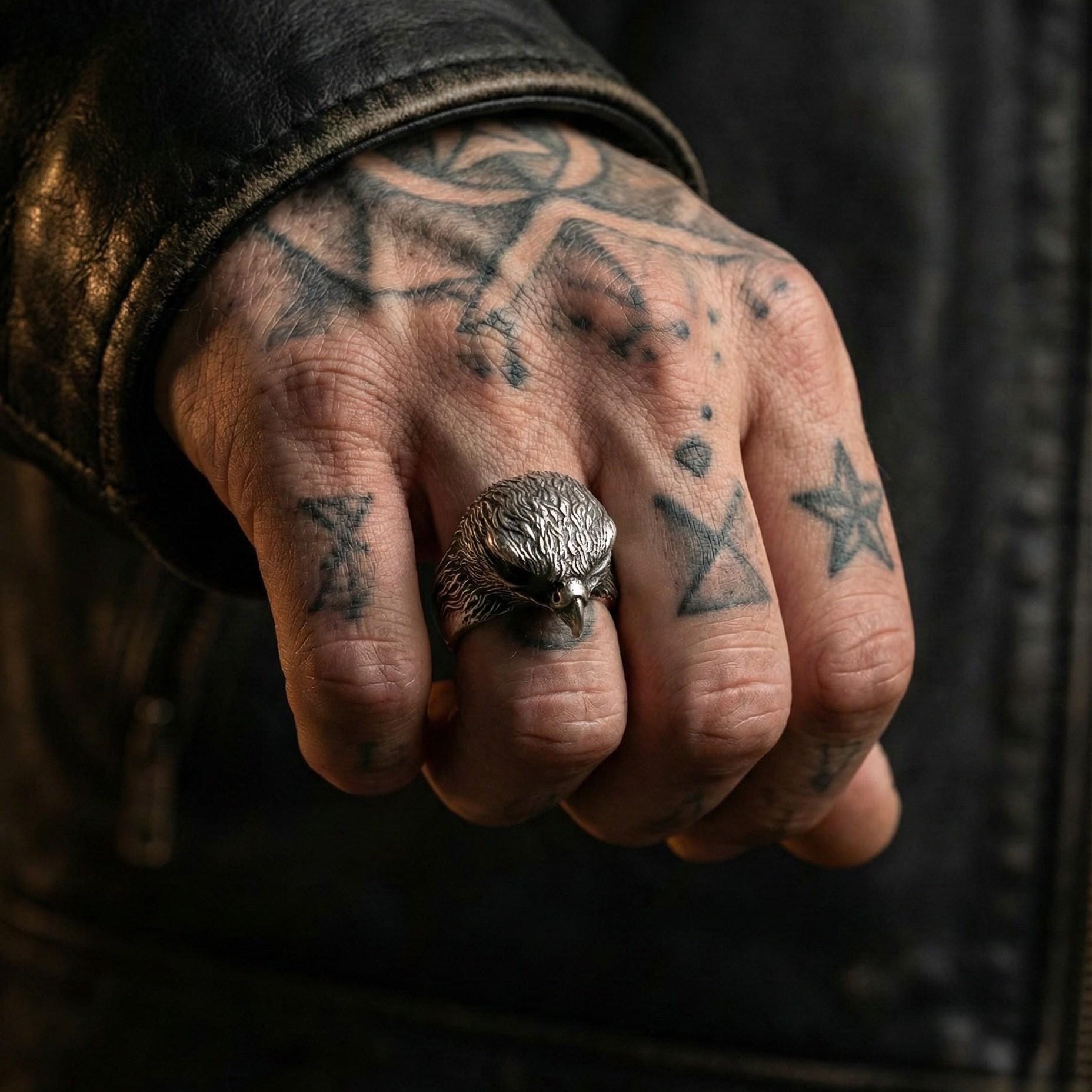 A close-up of a person's hand with tattoos on the fingers and a silver ring on the ring finger.
