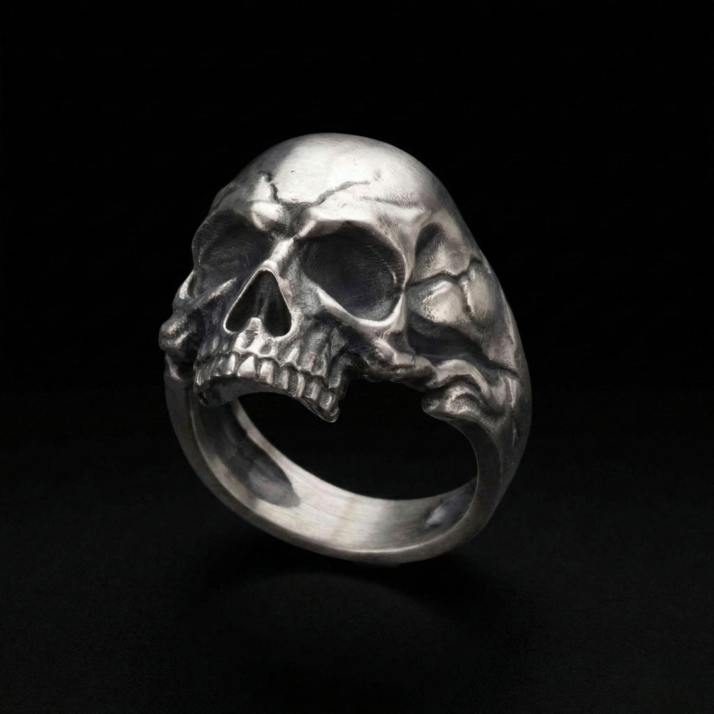 A silver skull ring is shown against a black background.