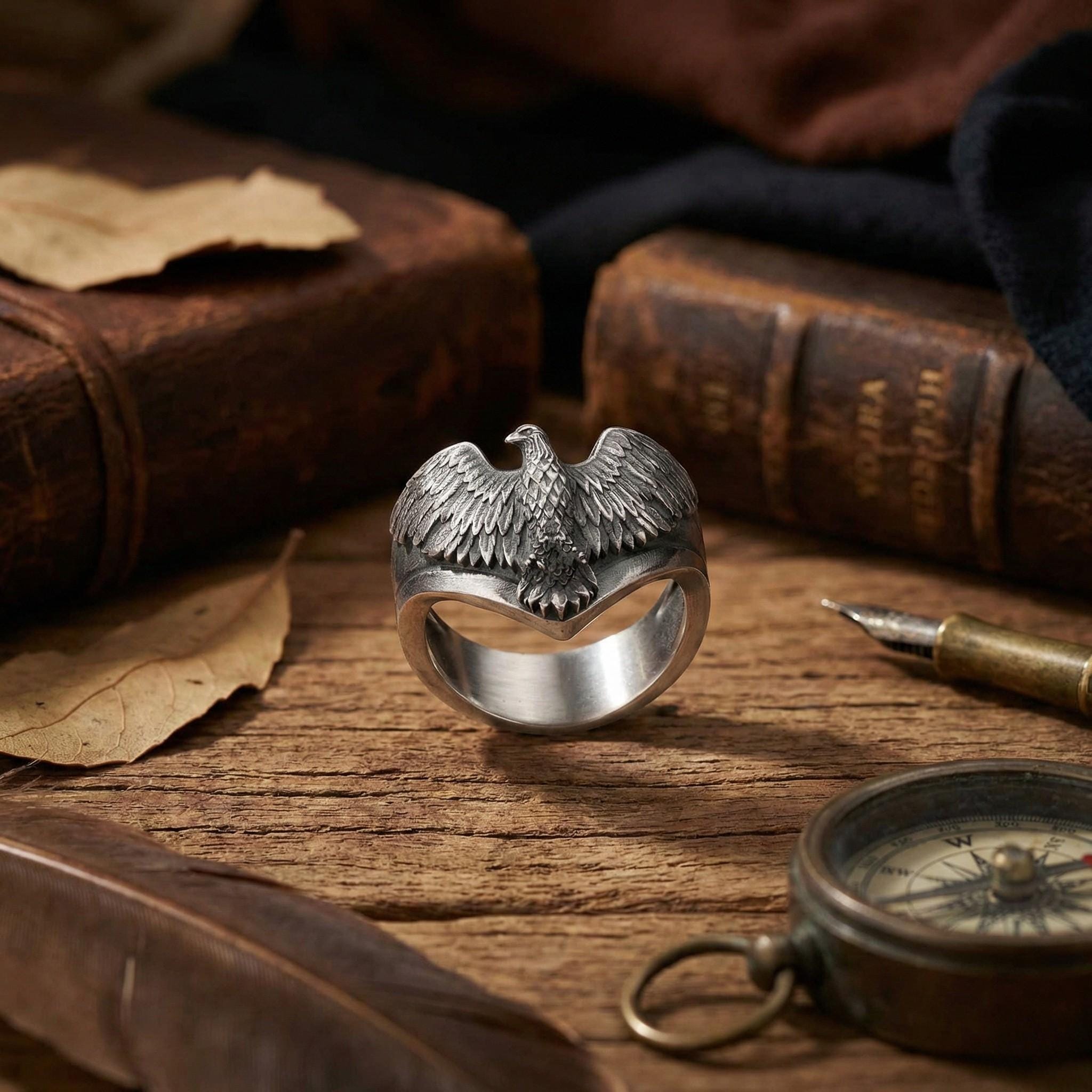 a silver ring with a bird design, surrounded by various objects such as a compass, a feather, and some books.