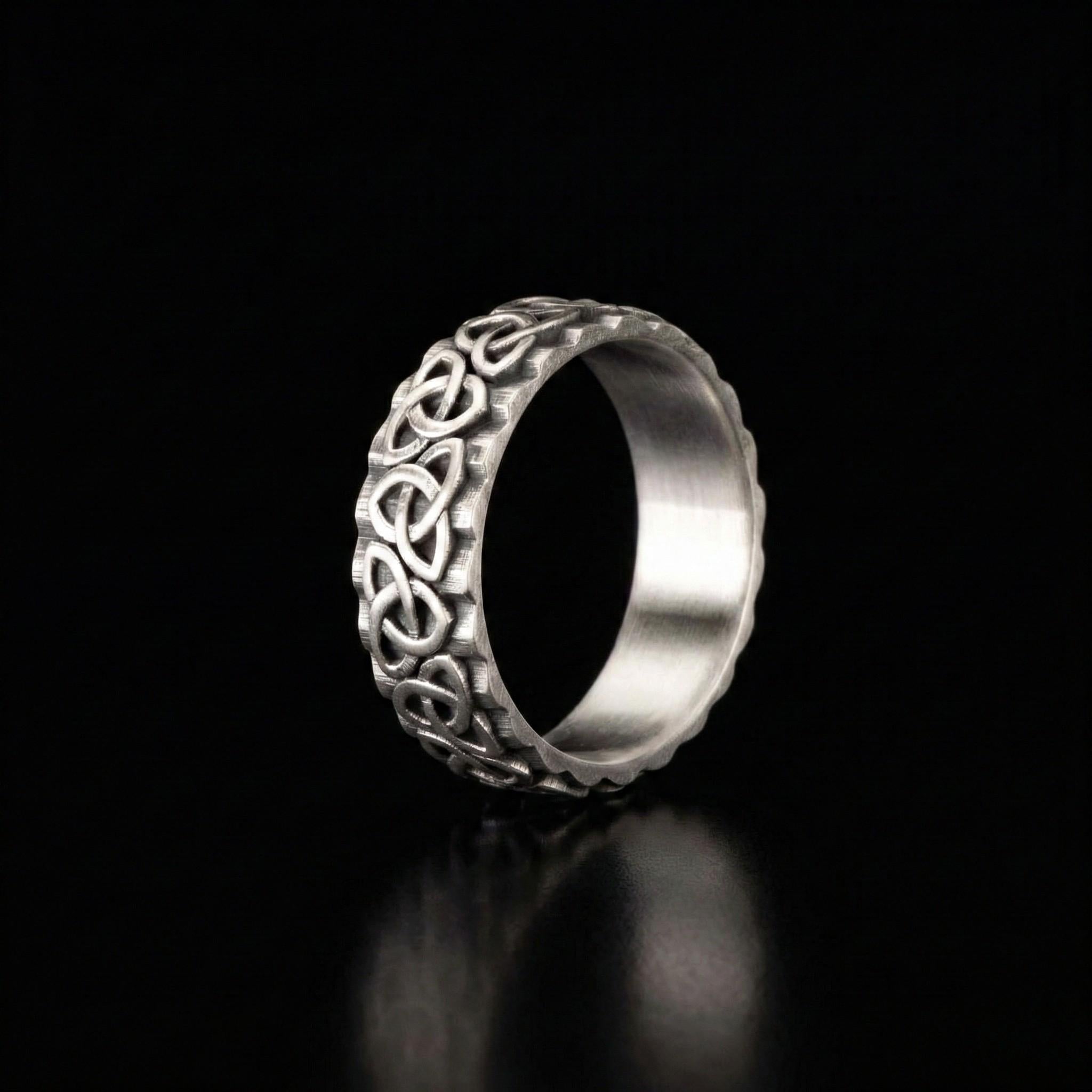 A silver ring with an intricate, decorative design on a black background.