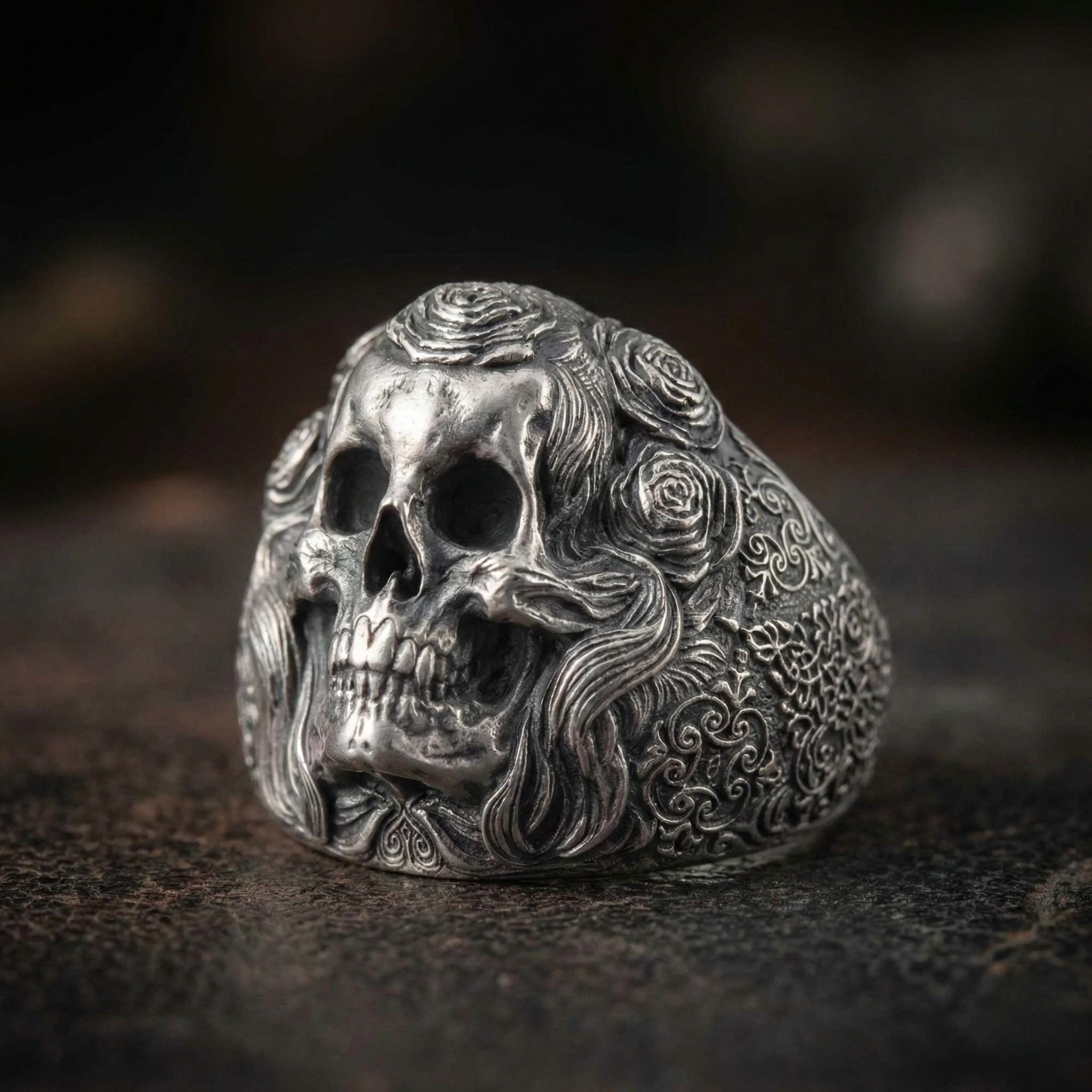 A silver ring with an intricate design featuring a skull and floral elements.