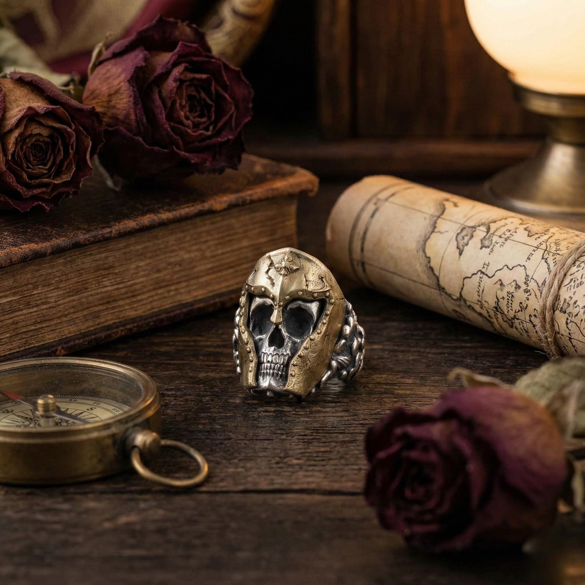 a ring with a skull design, a compass, a map, and two dried roses on a wooden surface.