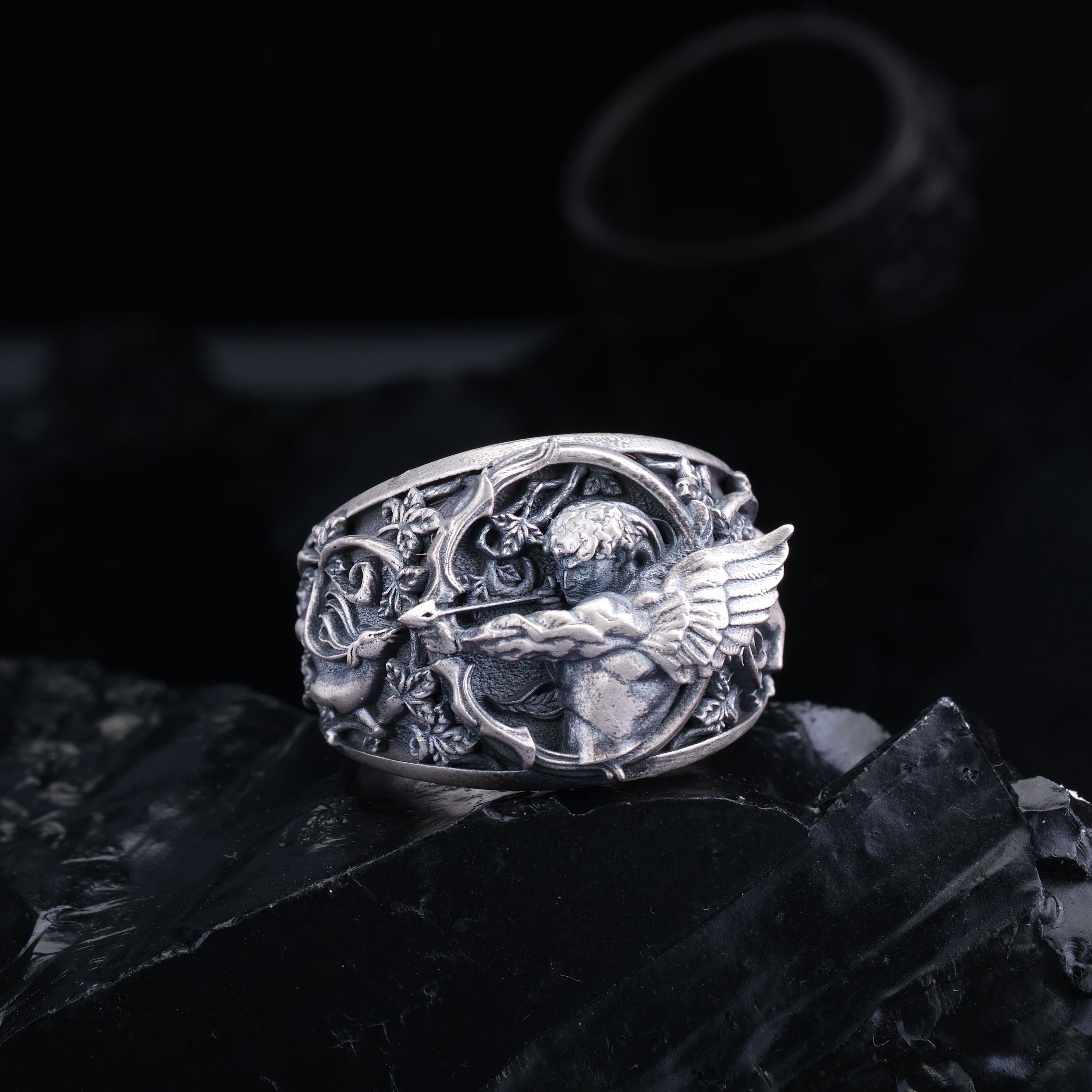 A silver ring with an intricate design featuring a winged creature, possibly a bird or a mythical creature, set against a dark background.