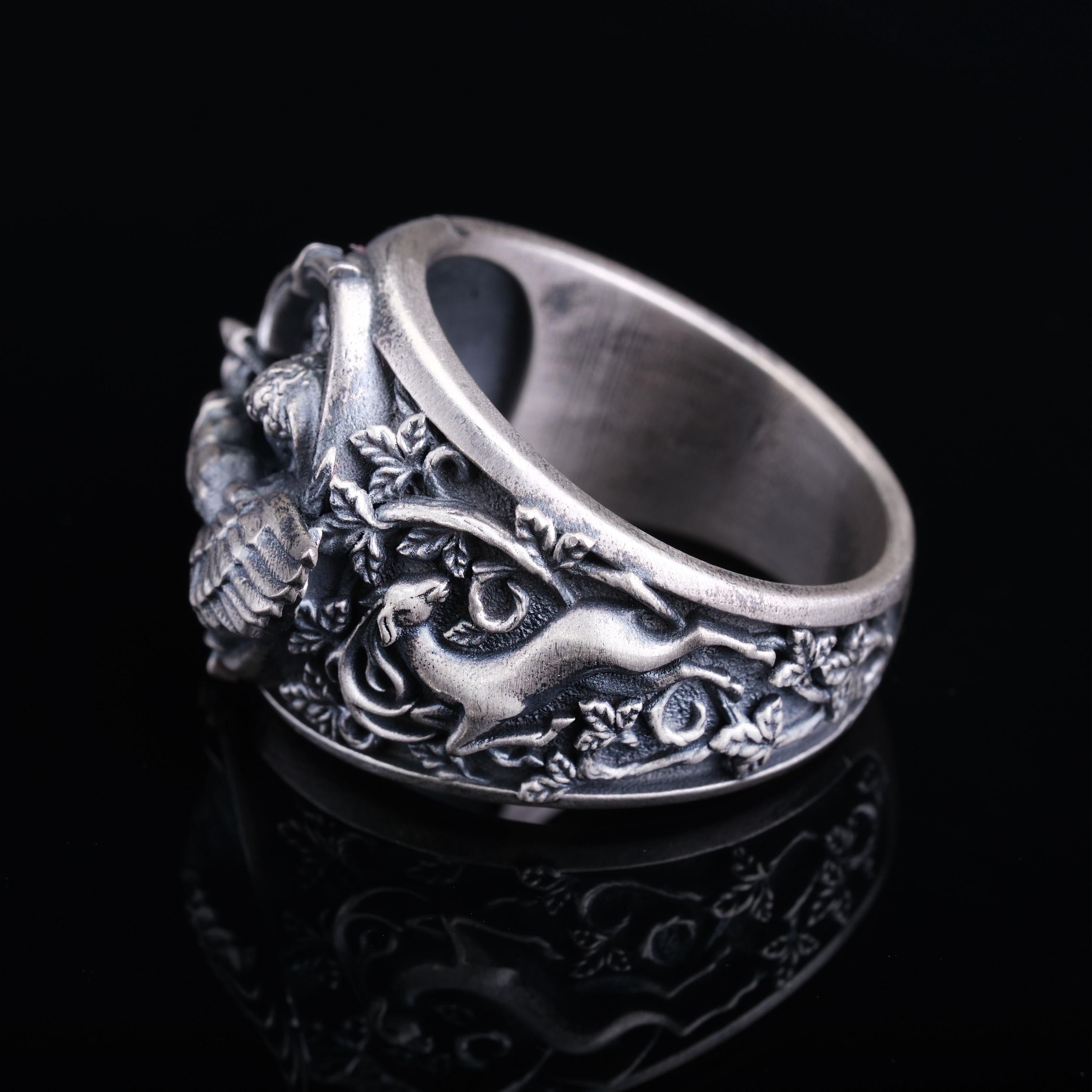 A silver ring with an intricate, embossed design featuring a bird and leaves.