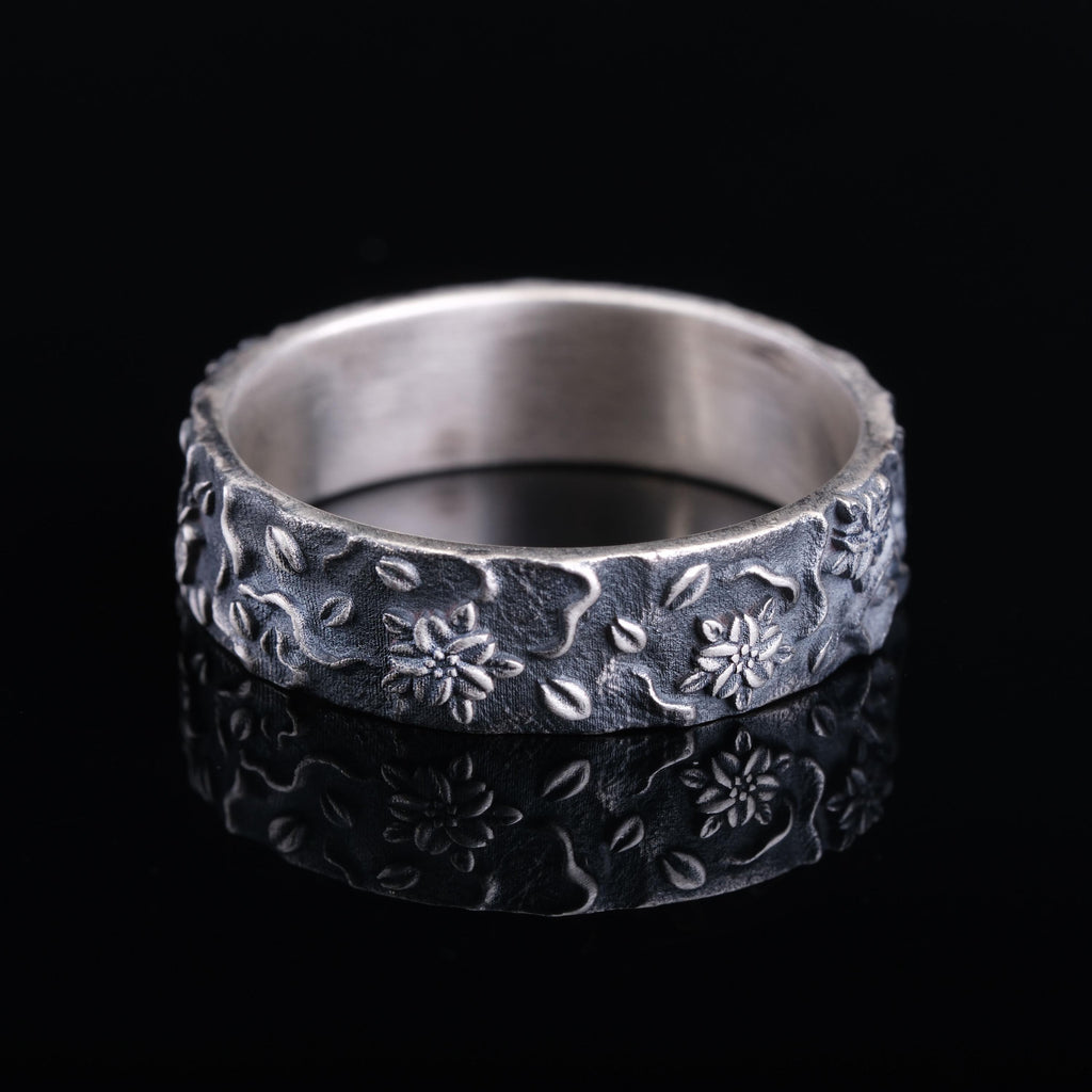 A silver ring with a floral design on a black background.