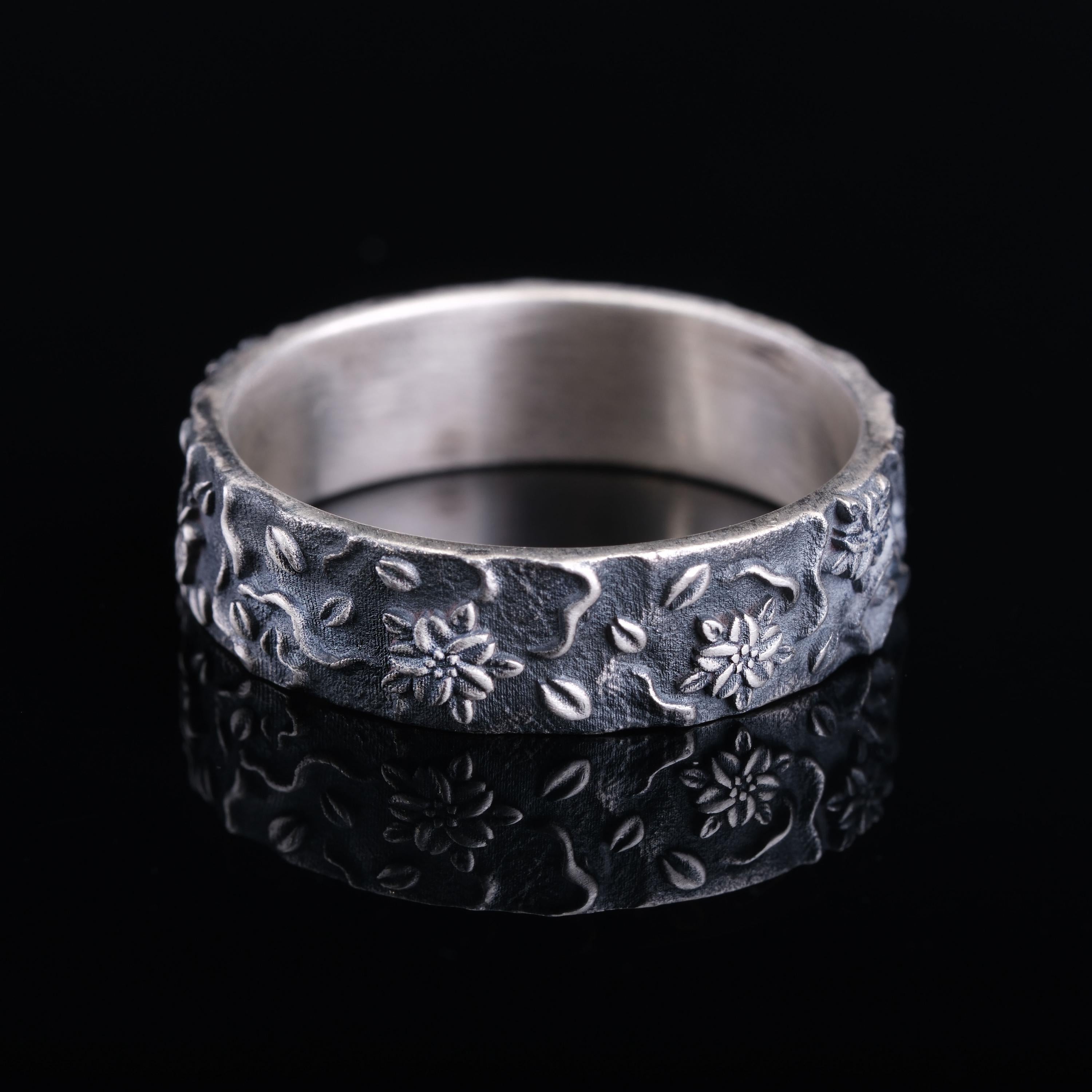A silver ring with a floral design on a black background.