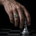 A hand wearing a ring is holding a chess piece, specifically a knight, on a chessboard.