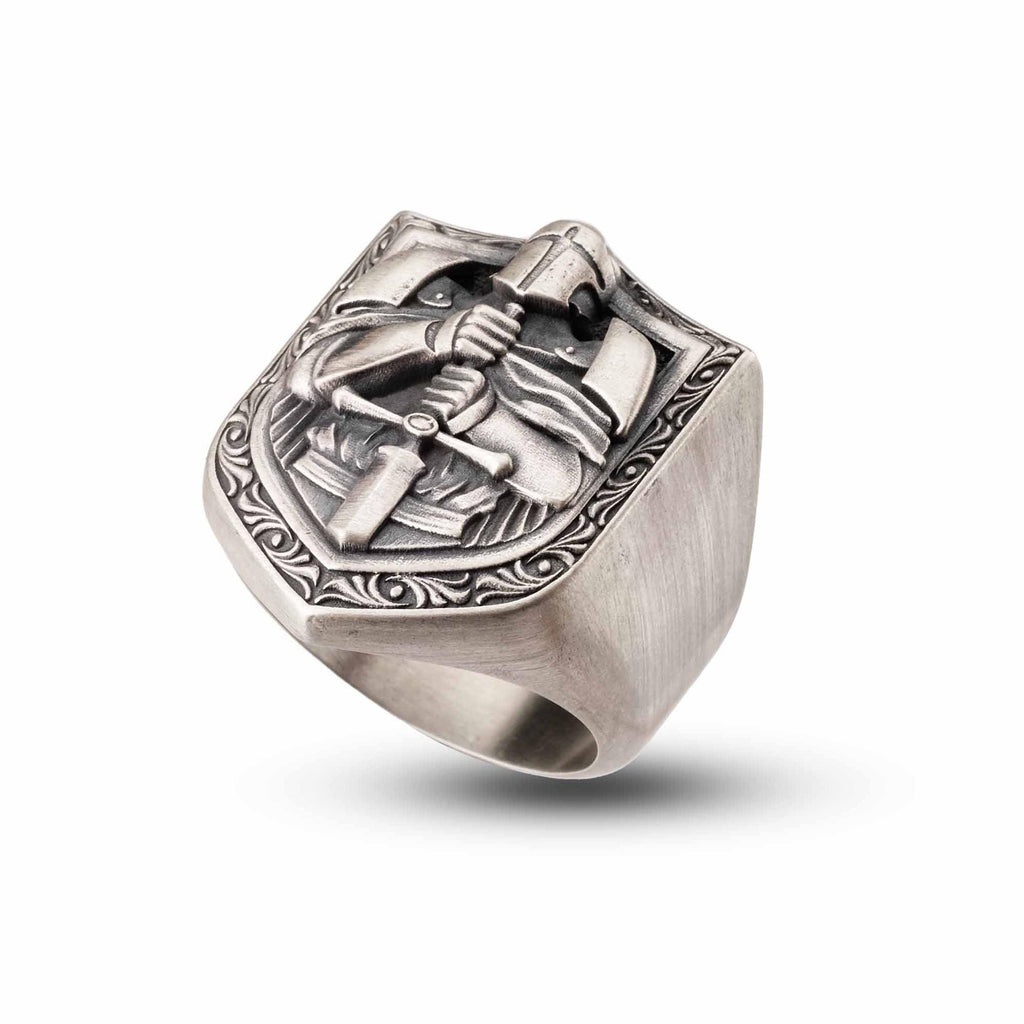 A silver ring with an intricate design featuring a shield-shaped motif and a figure holding a sword.