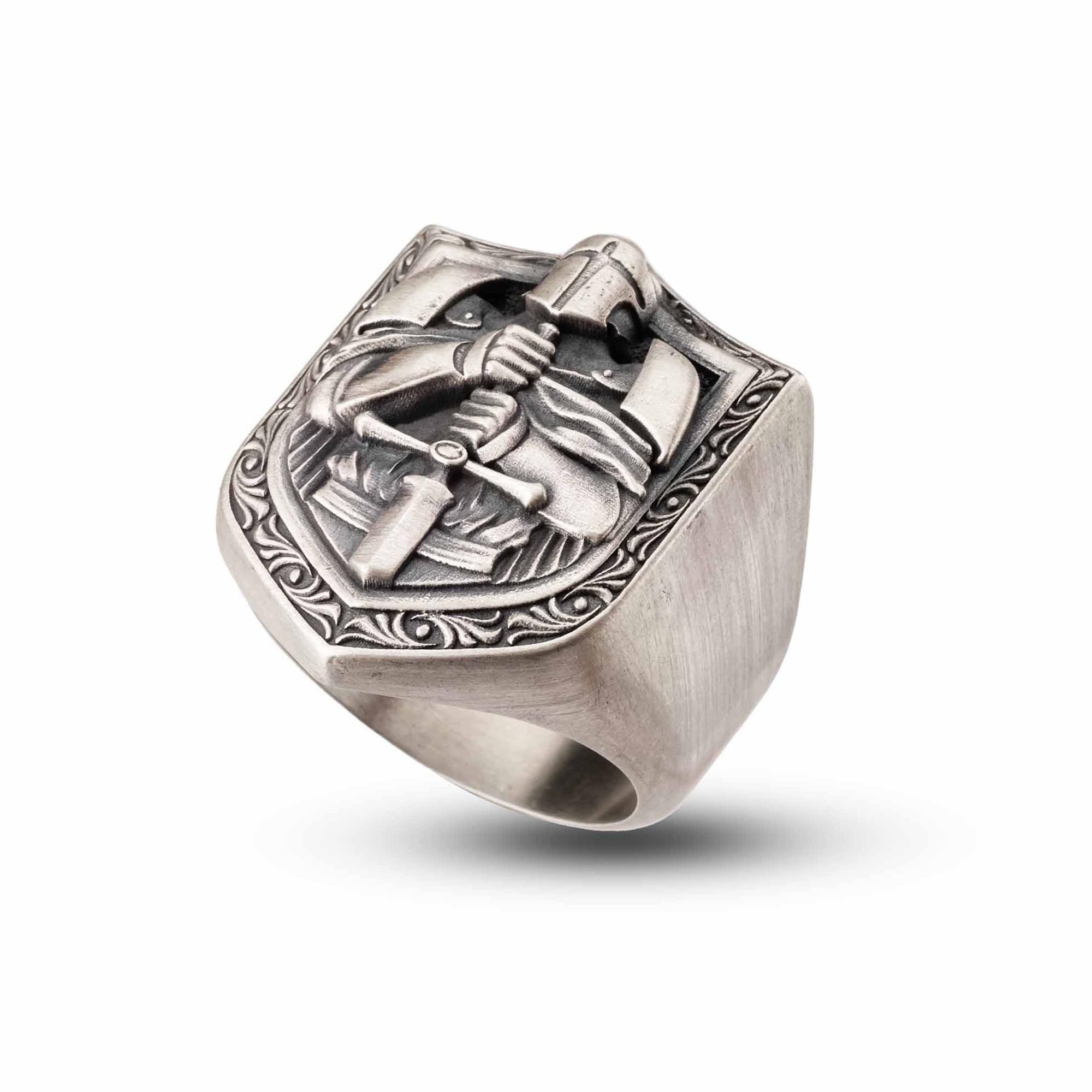 A silver ring with an intricate design featuring a shield-shaped motif and a figure holding a sword.
