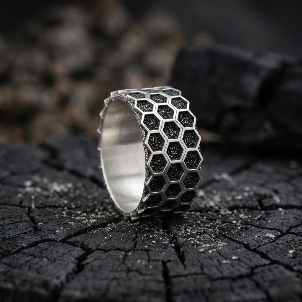 A silver ring with a honeycomb pattern sits on a dark, cracked surface.