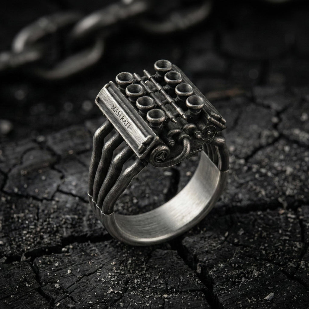 A silver ring with an intricate design, resembling an engine or machinery, is displayed on a dark, cracked surface.