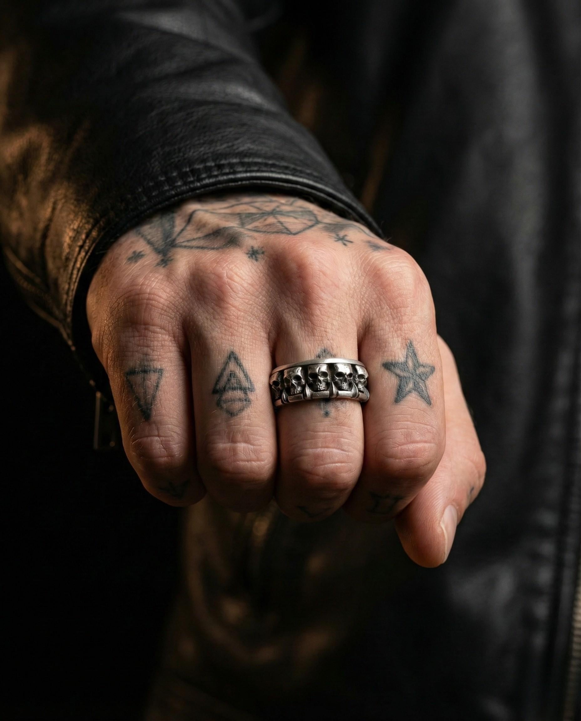A close-up of a person's hand with multiple tattoos on the fingers and a silver ring on the ring finger.
