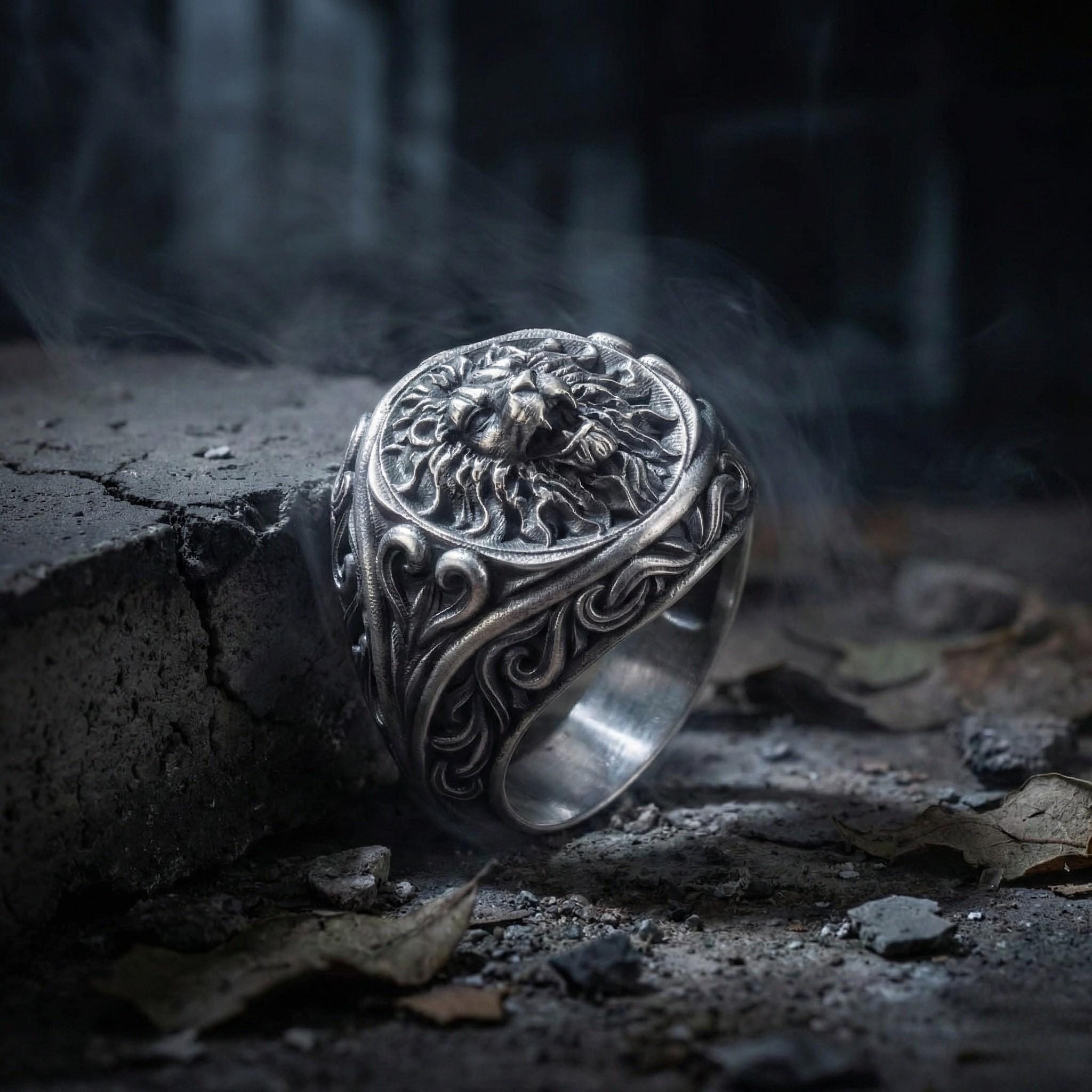 A silver ring with an intricate design sits on a rock, surrounded by a dark, moody background.