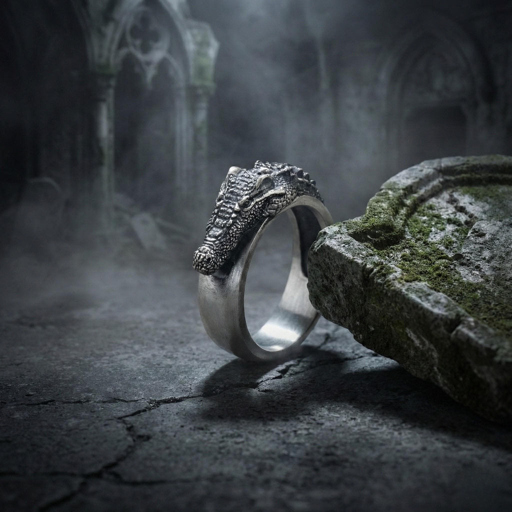 A silver ring with a dragon head design is resting on a moss-covered stone surface, with a dark, foggy background.