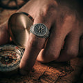 A close-up of a person's hand wearing a silver ring with a compass design, resting on a map.