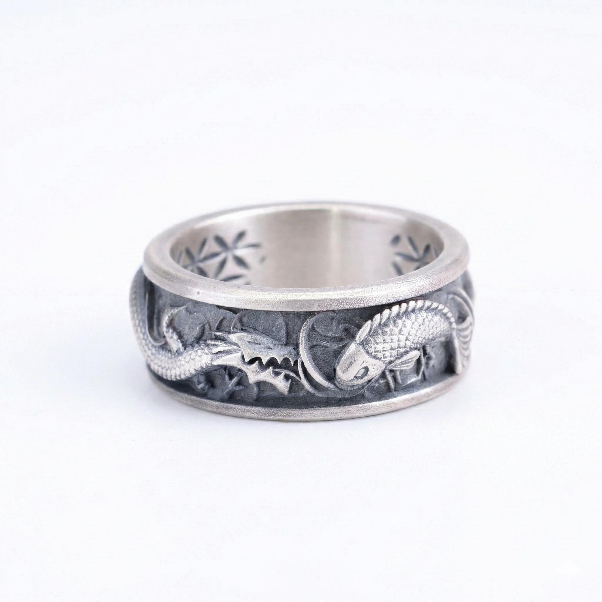 A silver ring with an intricate design featuring a dragon and a fish.