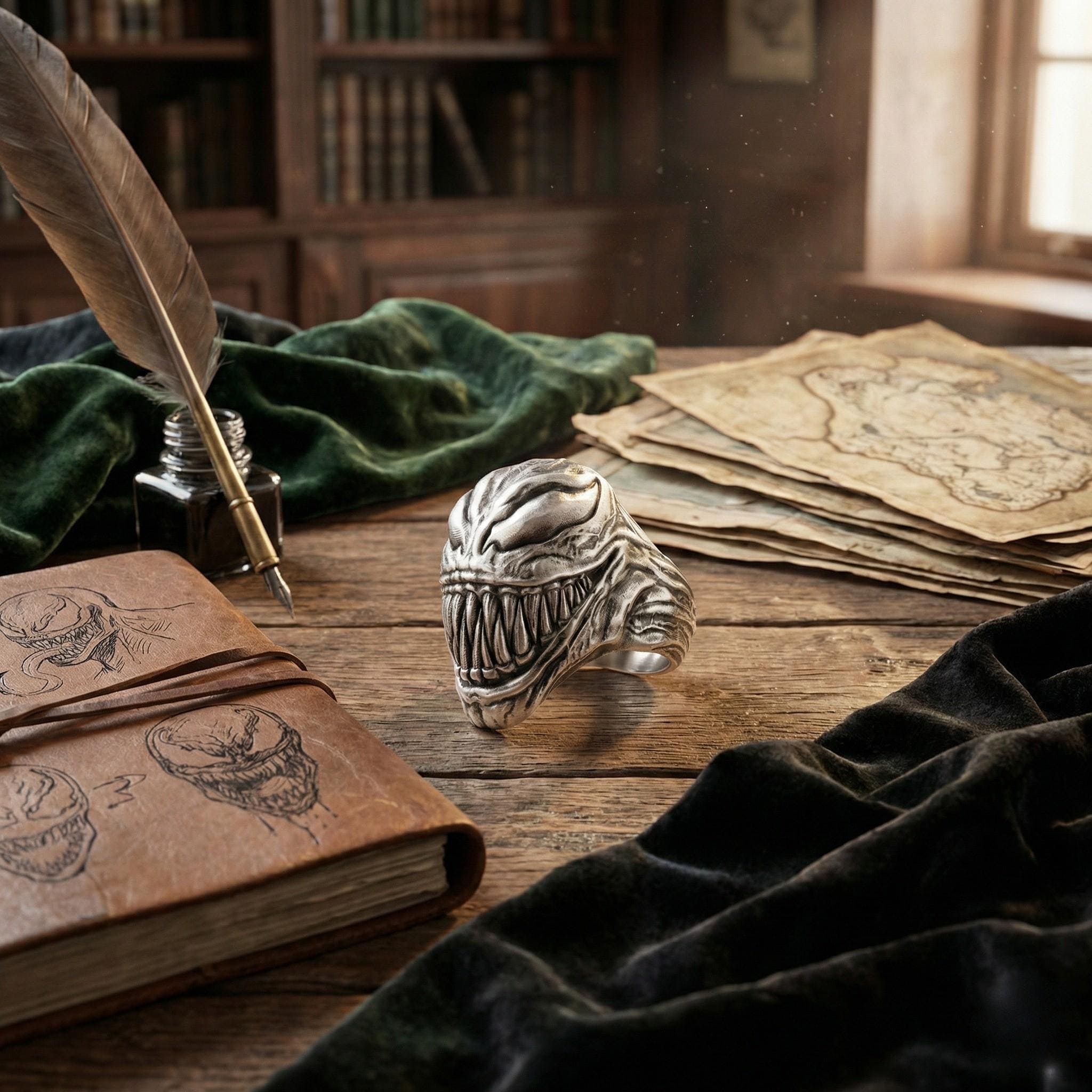 a ring with a menacing design, a notebook with a skull and crossbones motif, a feather quill pen, and a stack of papers with a map on top, all arranged on a wooden surface.