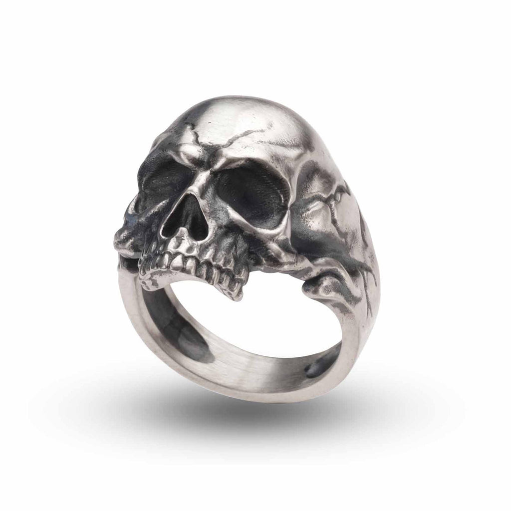 A silver ring in the shape of a skull with a carved design.