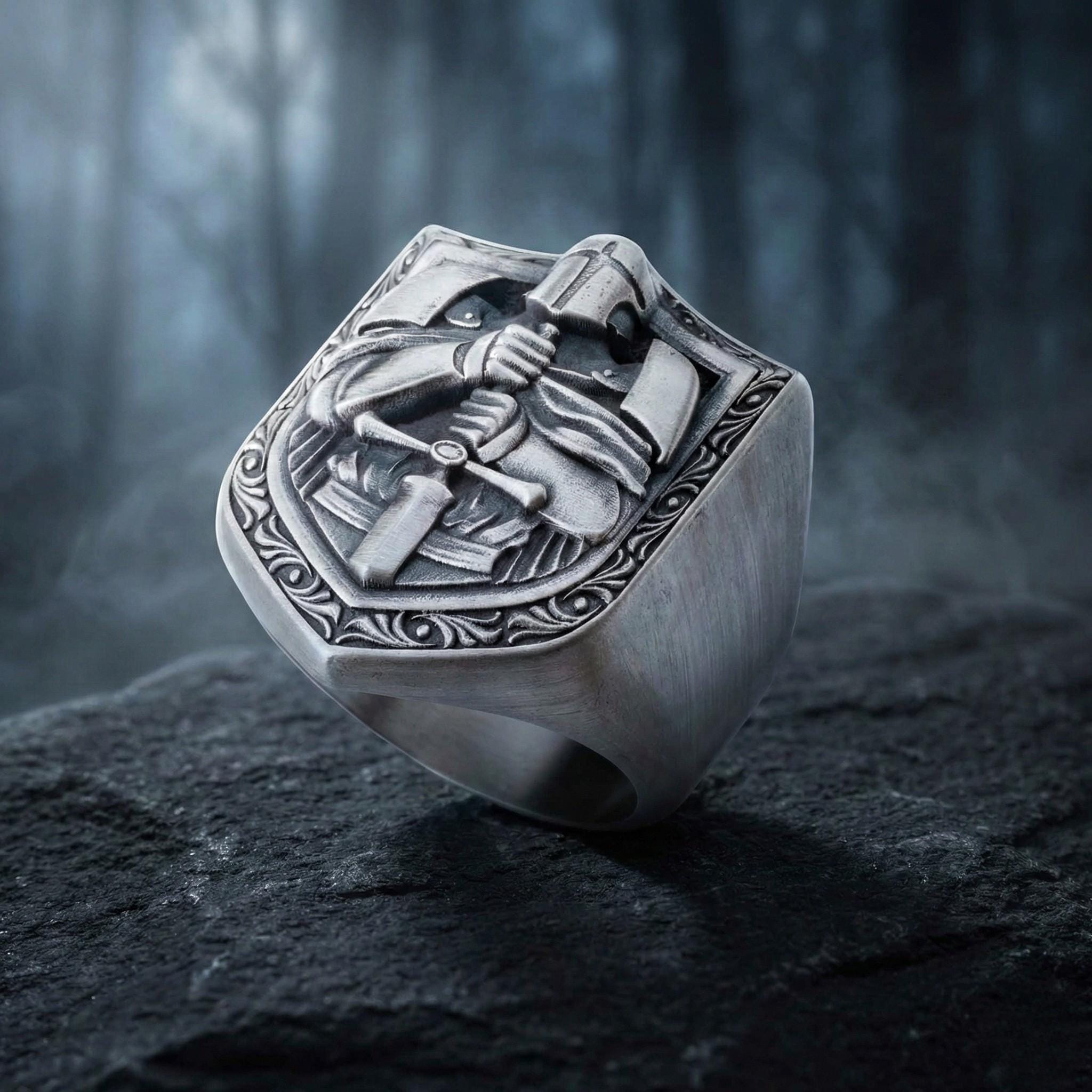 A silver ring with an intricate design featuring a shield-shaped motif, possibly a symbol of protection or authority.