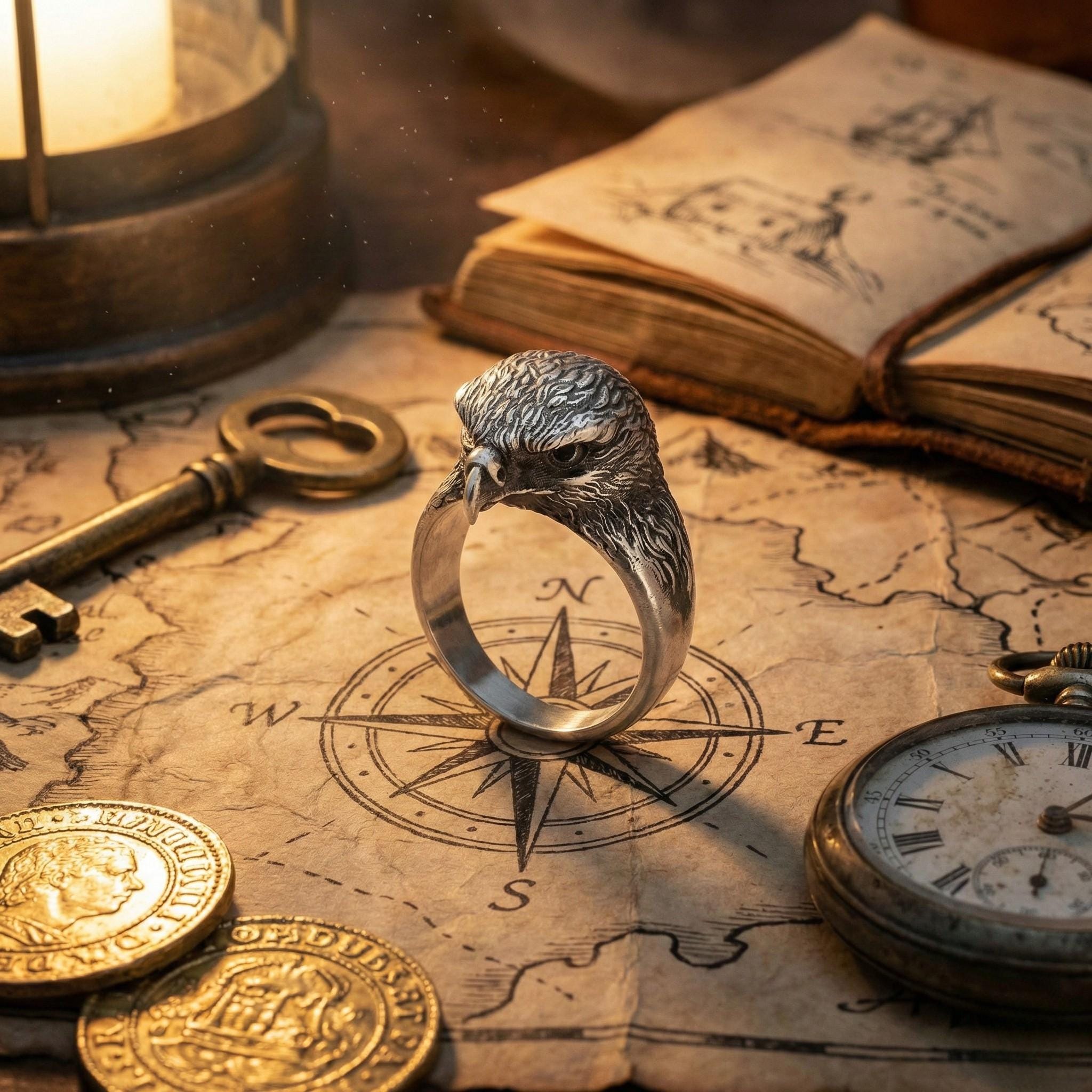 a silver ring with a bird head design, surrounded by various objects such as a key, a compass, and an open book.