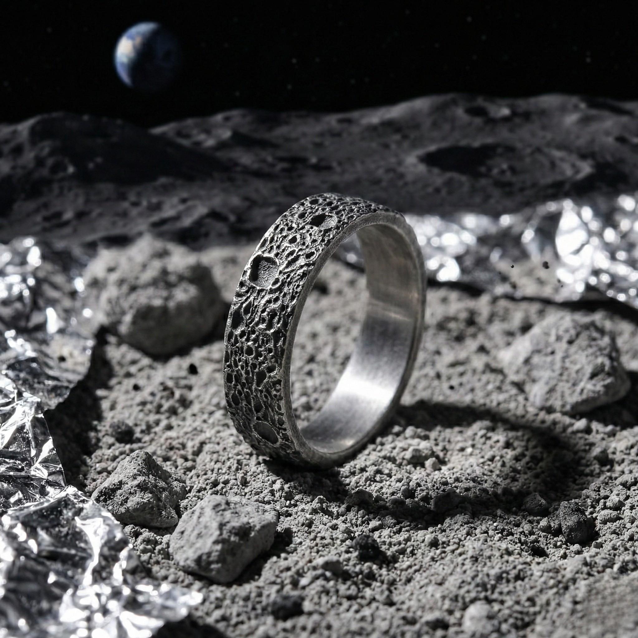 A silver ring with a textured surface sits on a rocky surface, with a planet visible in the background.