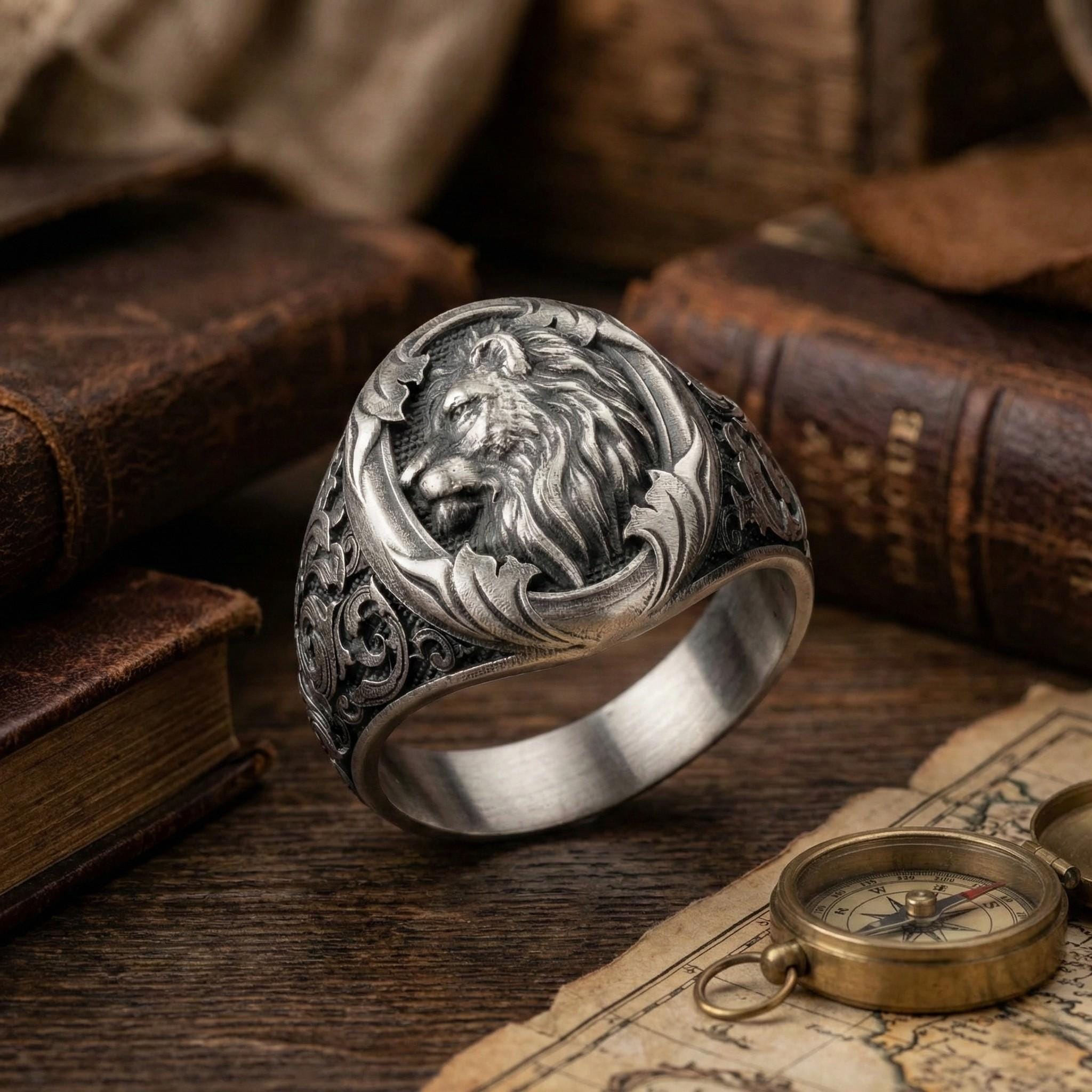 a silver ring with an intricate design, placed on a wooden surface next to a compass and some books.