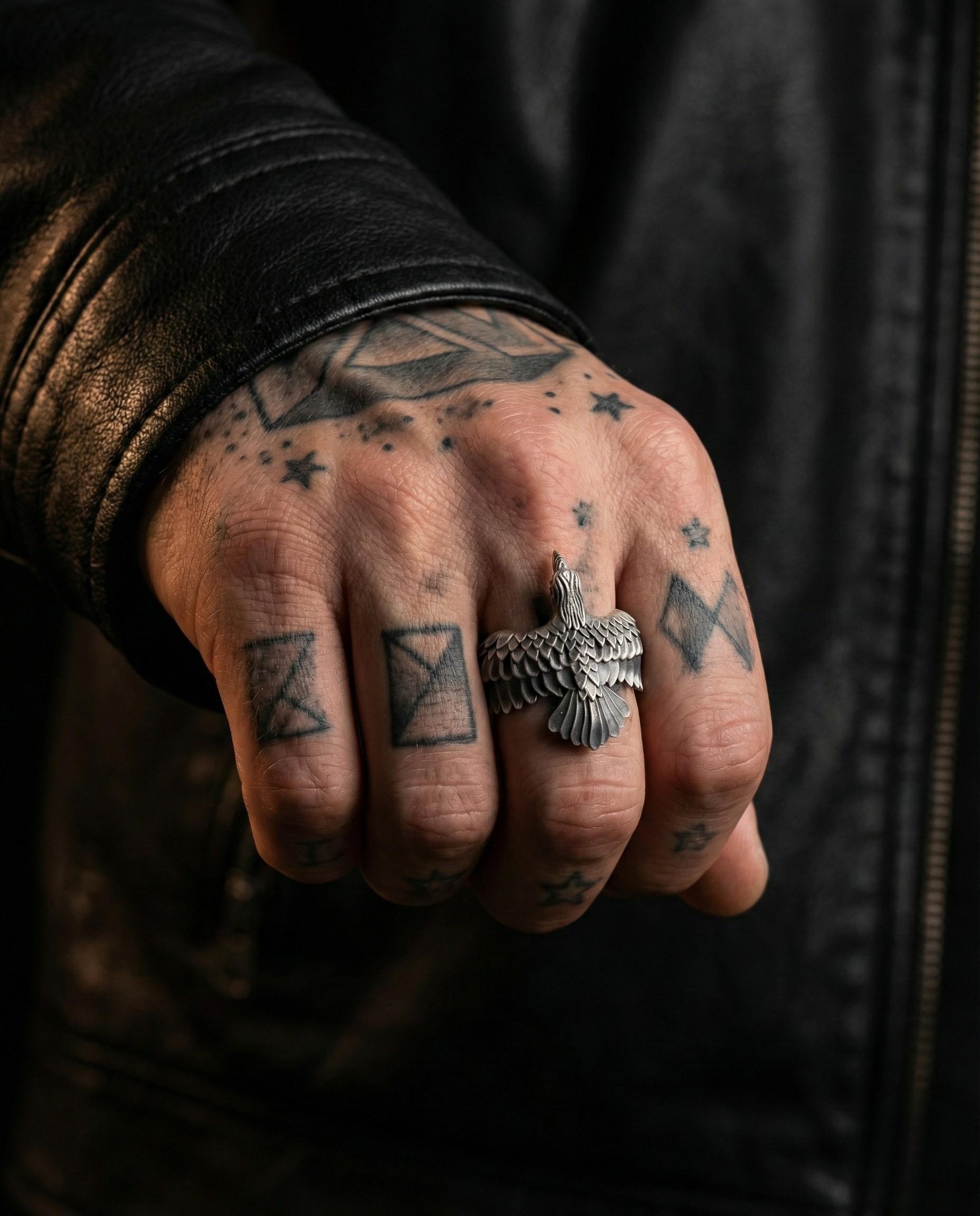 A close-up of a person's hand with tattoos on the fingers and a silver ring on the ring finger.