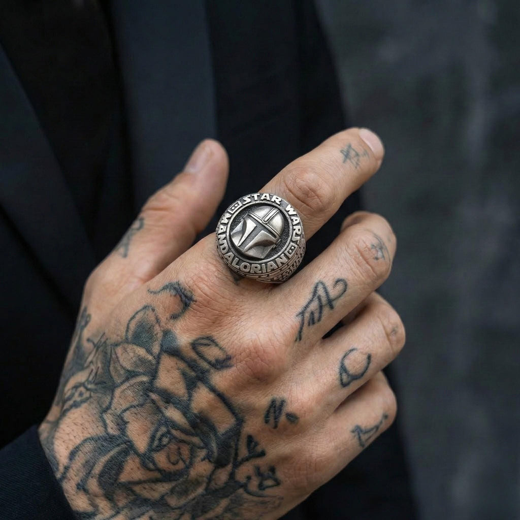 A close-up of a person's hand with a large ring on one finger and tattoos on the other fingers.
