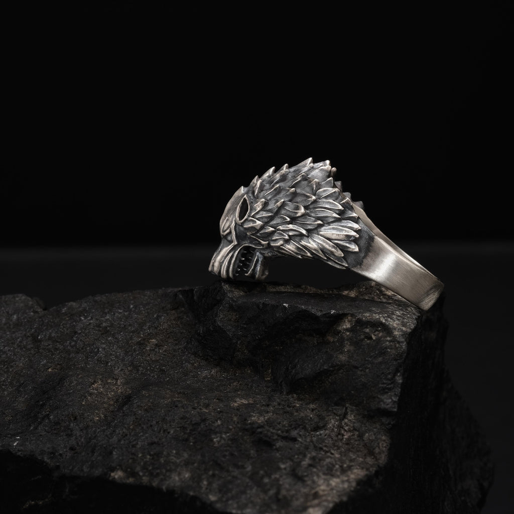 A silver ring with a detailed wolf head design is resting on a dark, rocky surface.