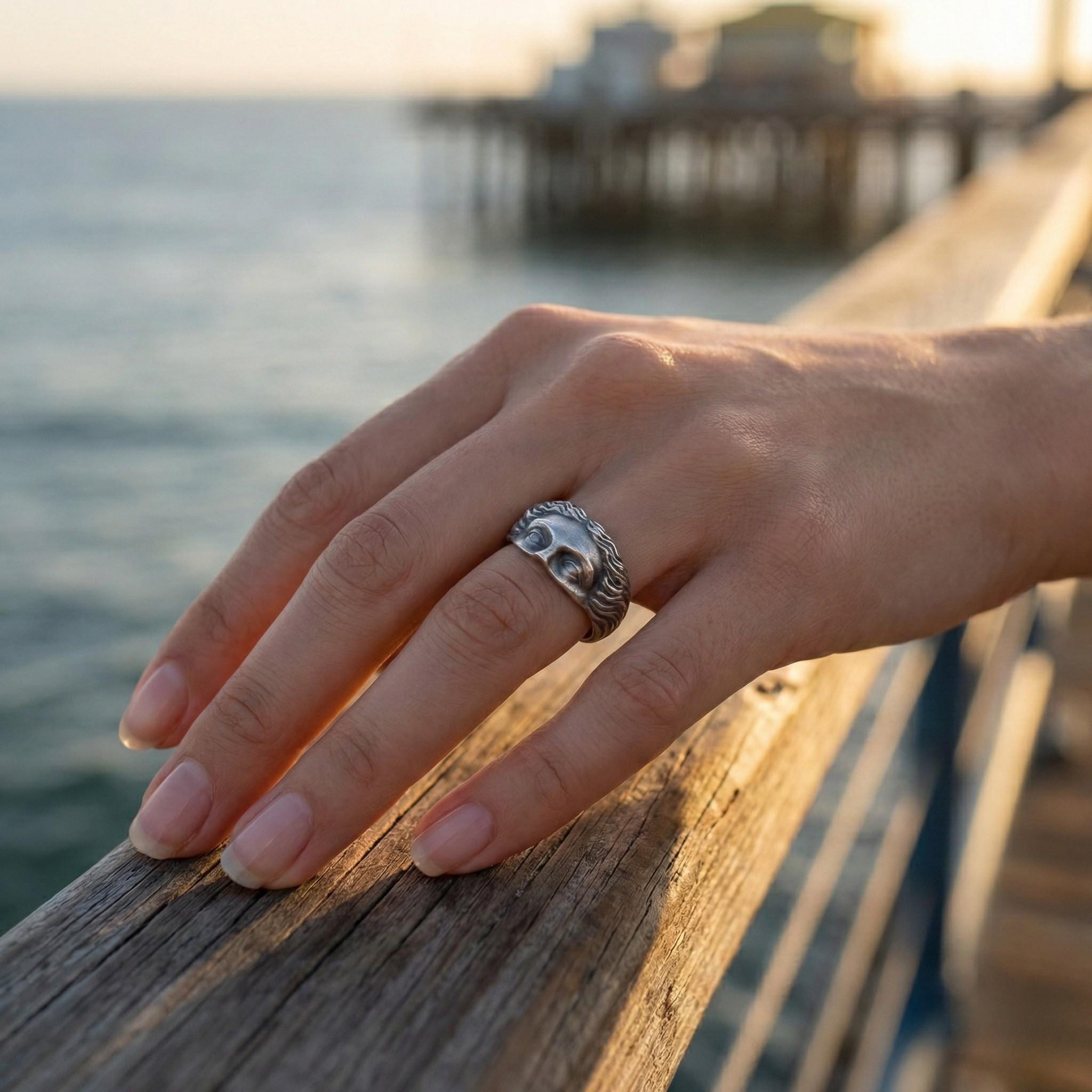 A close-up of a hand wearing a silver ring resting on a wooden railing, with a body of water and a pier in the background.