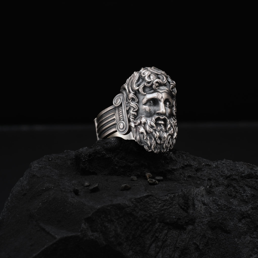 A silver ring with an intricate design sits on a dark surface, possibly a rock or a stone.