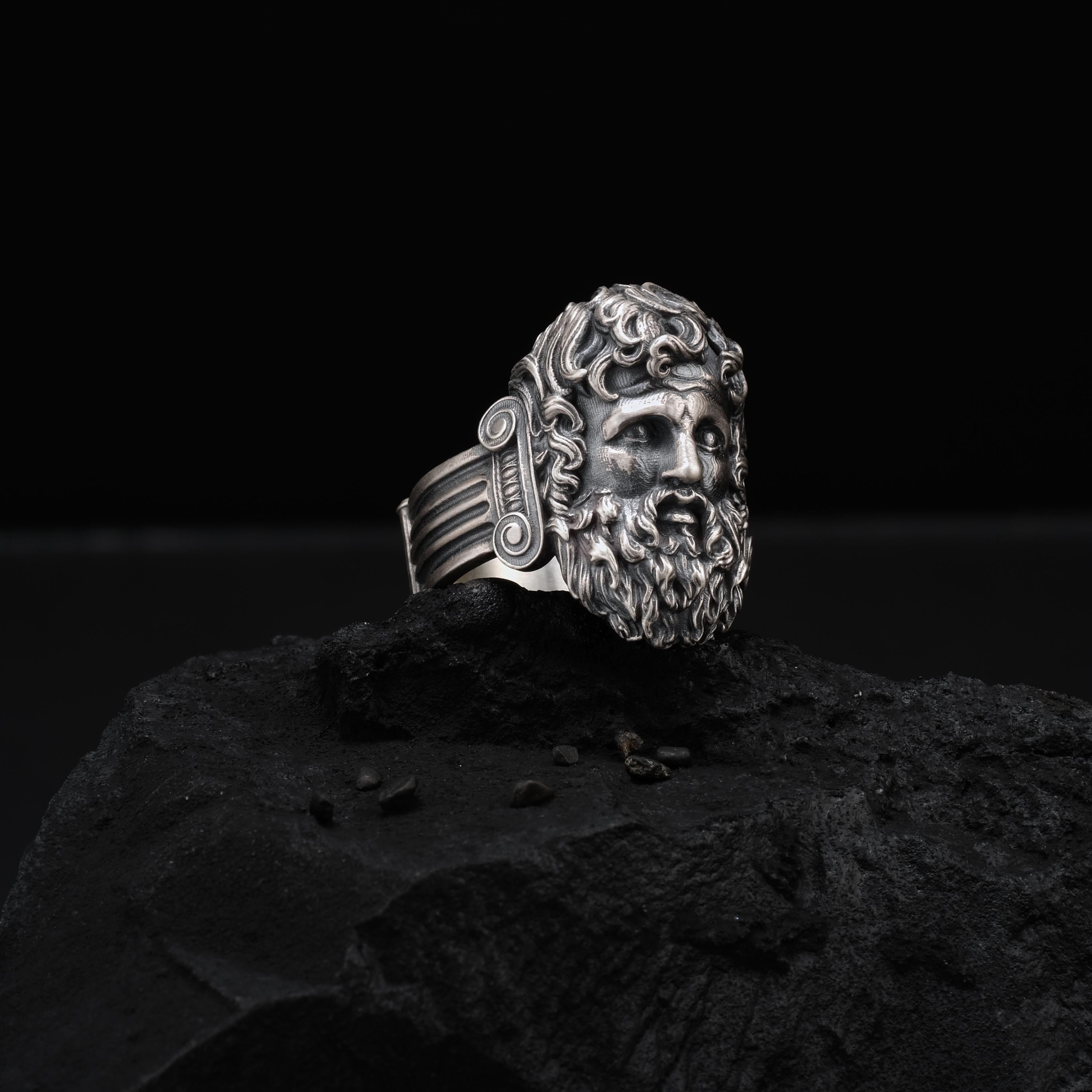 A silver ring with an intricate design sits on a dark surface, possibly a rock or a stone.