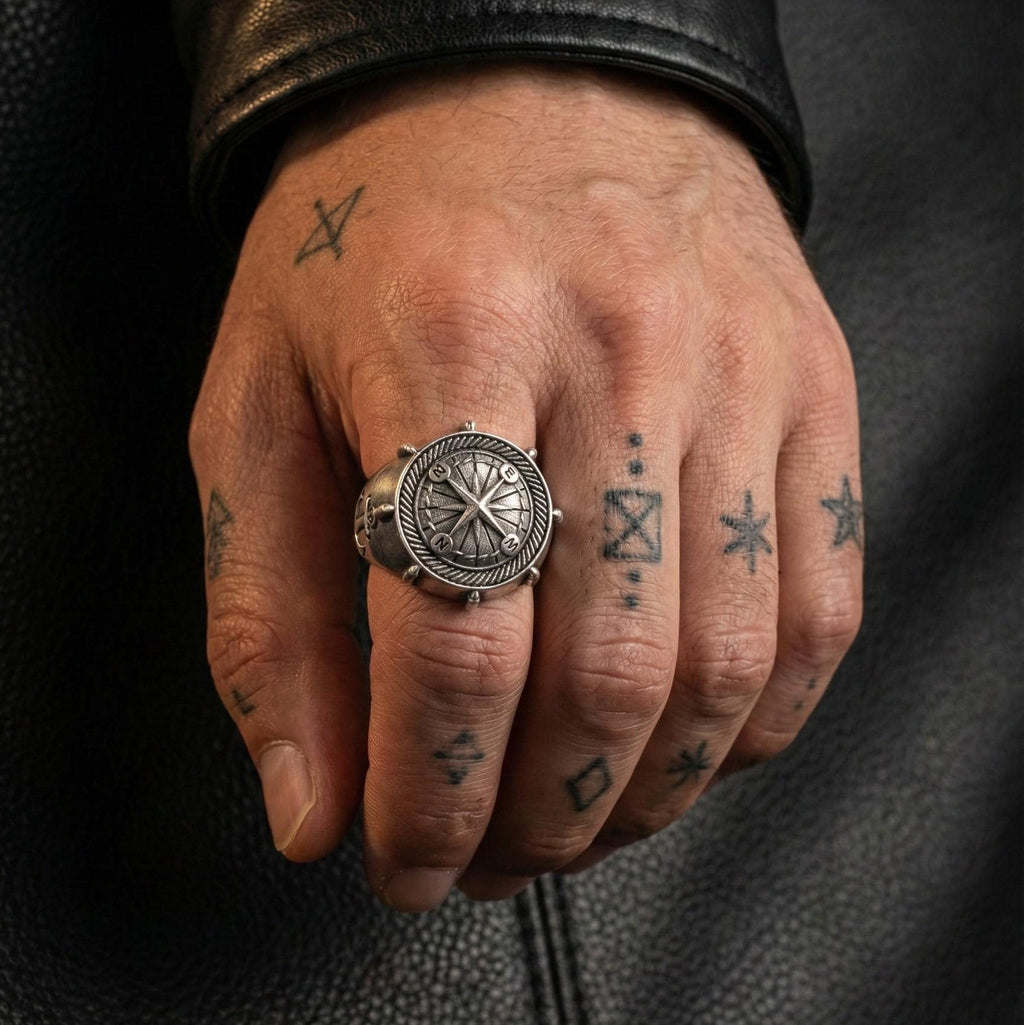 A close-up of a person's hand wearing a silver ring with a decorative design, and multiple tattoos on the fingers.