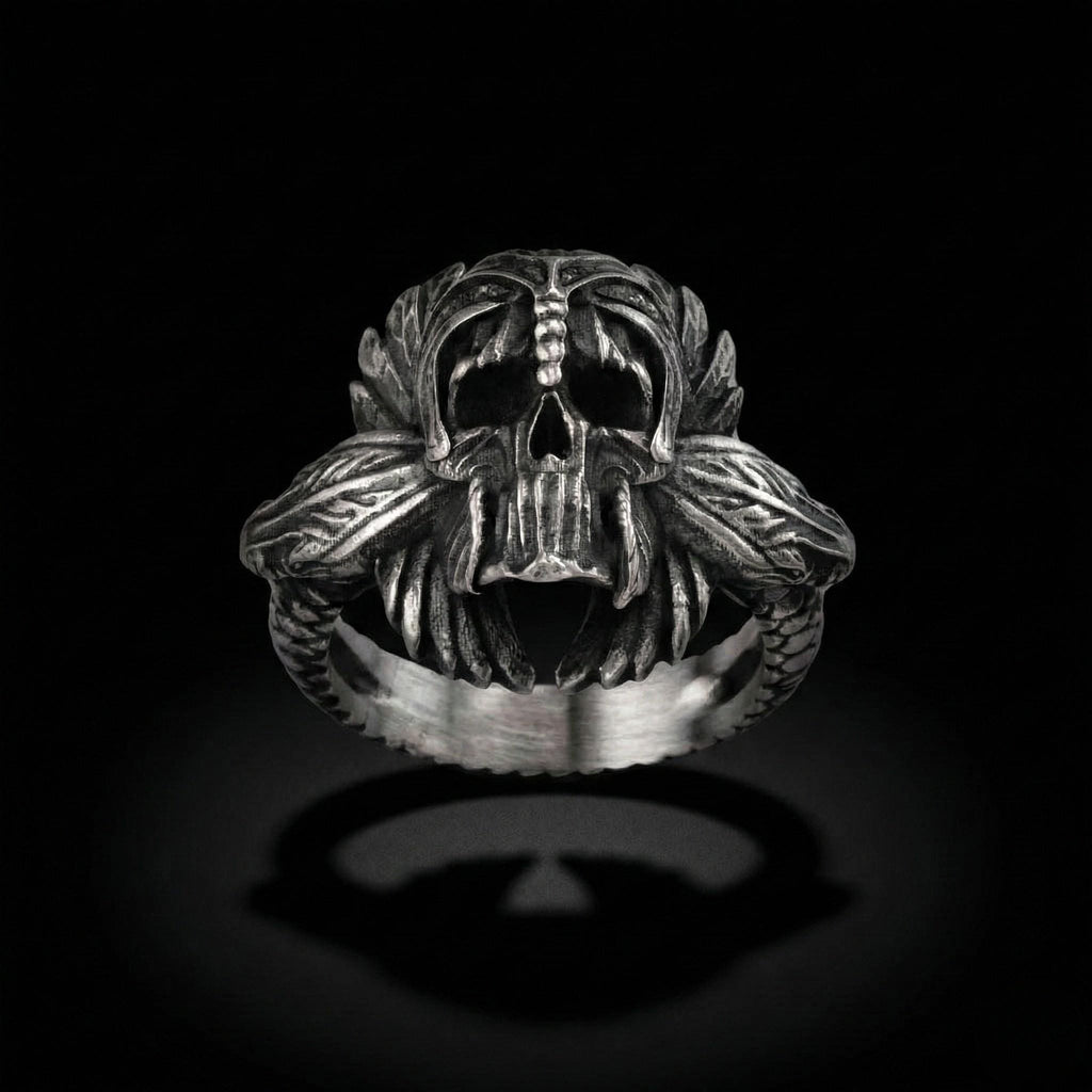 A silver ring with an intricate design featuring a skull and two snakes.