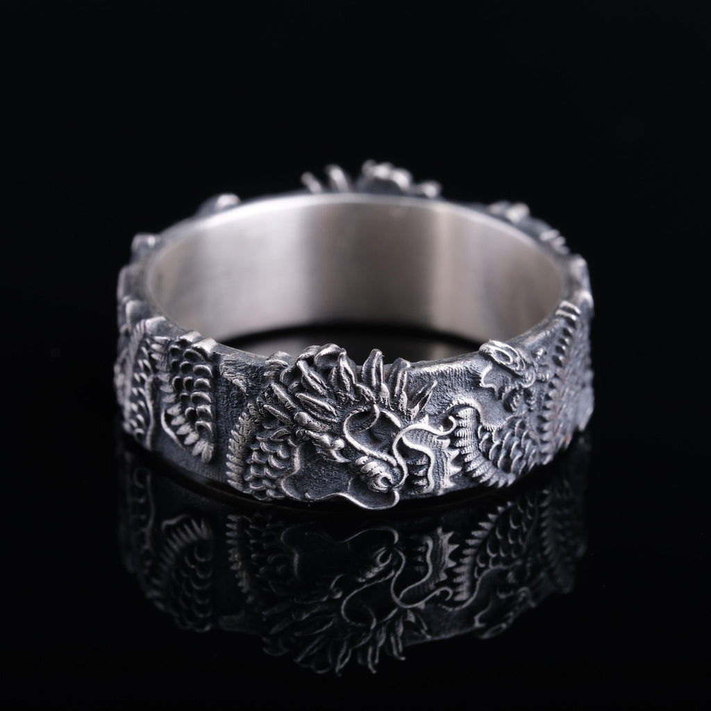 A silver ring with an intricate dragon design on a black background.