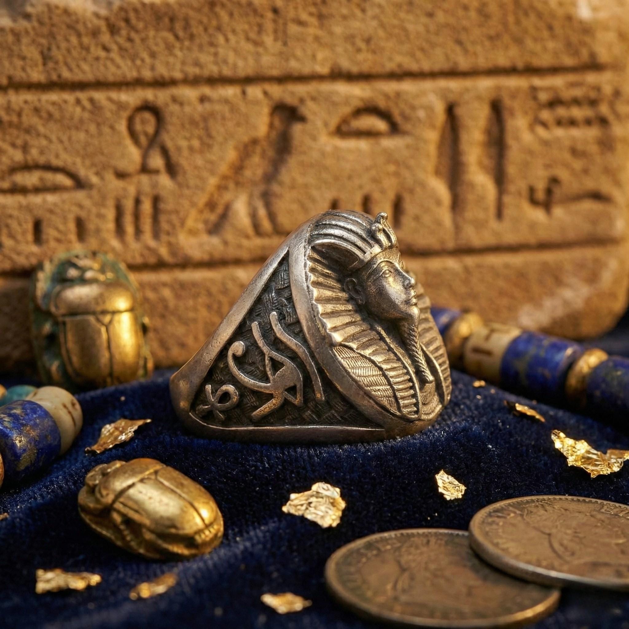 a ring with a pharaoh's head design, surrounded by various ancient Egyptian artifacts such as coins, a scarab, and a hieroglyphic stone.