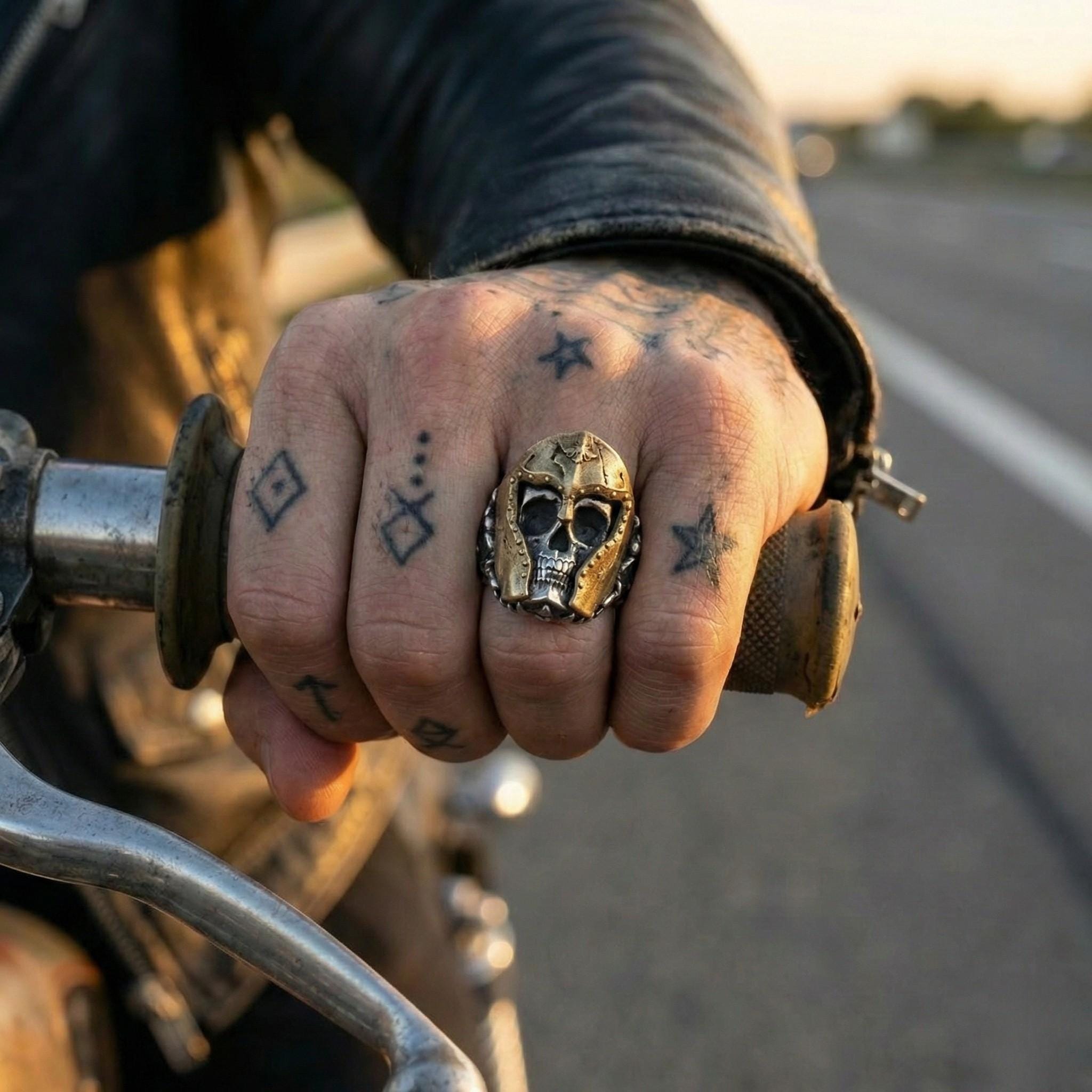 A close-up of a person's hand wearing a ring with a skull design, holding a motorcycle handlebar.